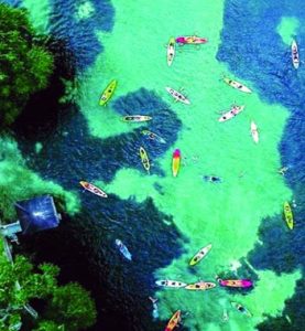 A top-down view of clear turquoise waters dotted with colorful kayaks, suggesting a serene day of paddling in a vibrant aquatic landscape.