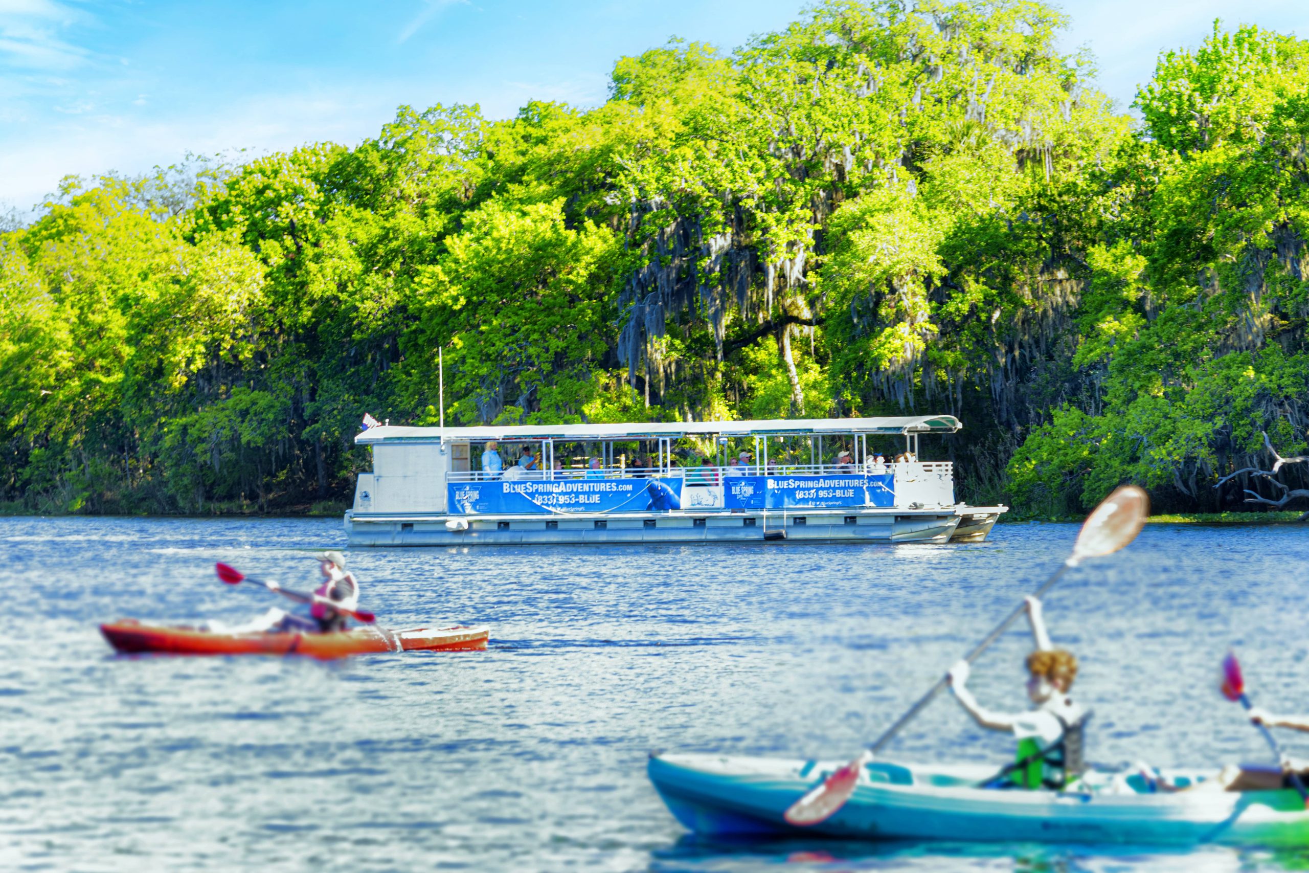 Sightseeing boat on the river with kayakers in the foreground.