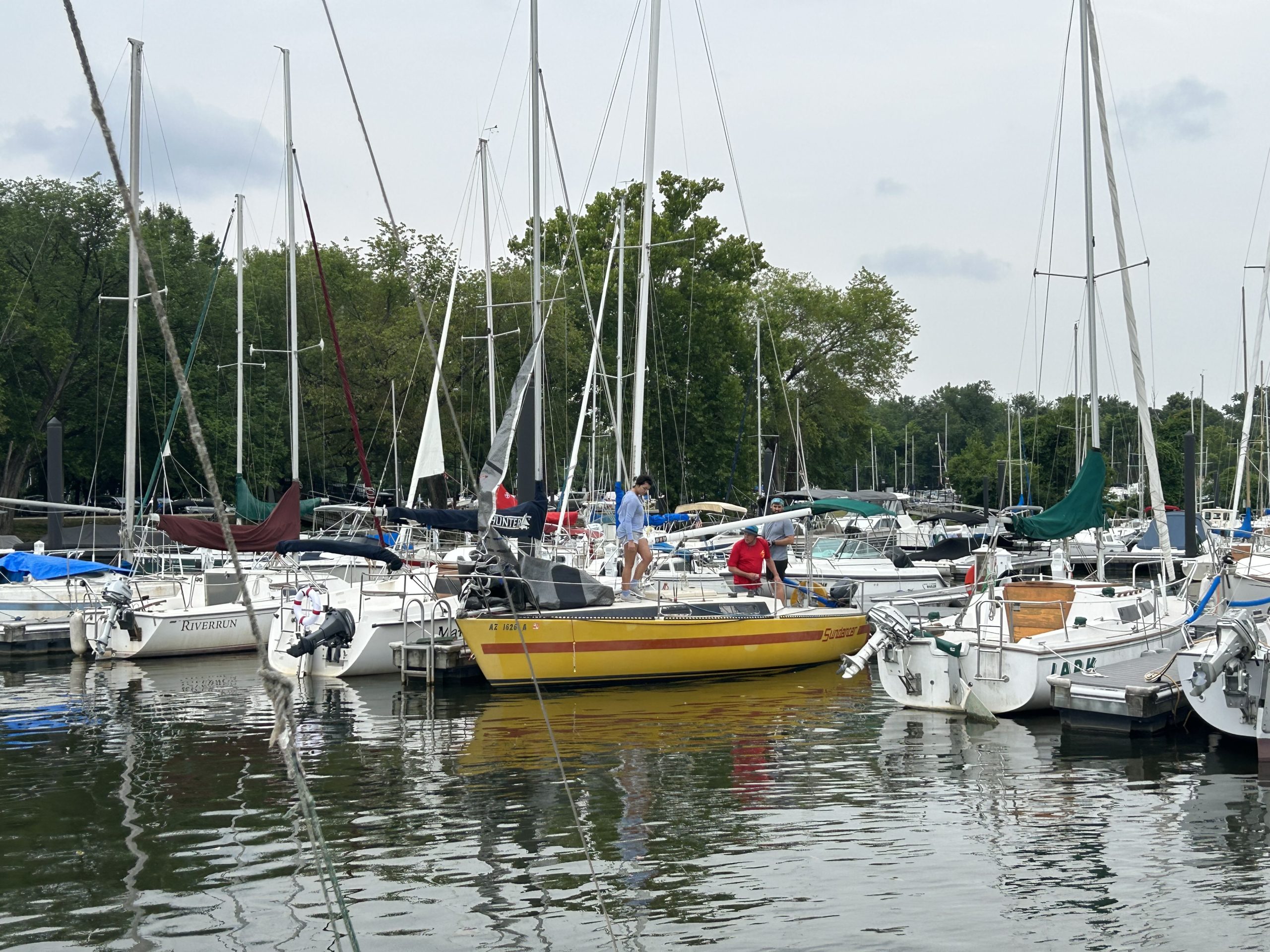 Marina full of sailboats and a yellow motorboat on calm water.