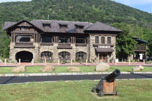 Front view of the historic Bear Mountain Inn with stone architecture, wooden beams, and a cannon set against lush green hills