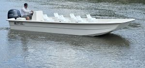 Man driving a Carolina Skiff E24 DLX boat on calm waters that is used for boat tours in florida, with multiple white seats for passengers.
