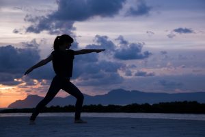 Woman doing yoga on a beach at sunset during a wellness trip.