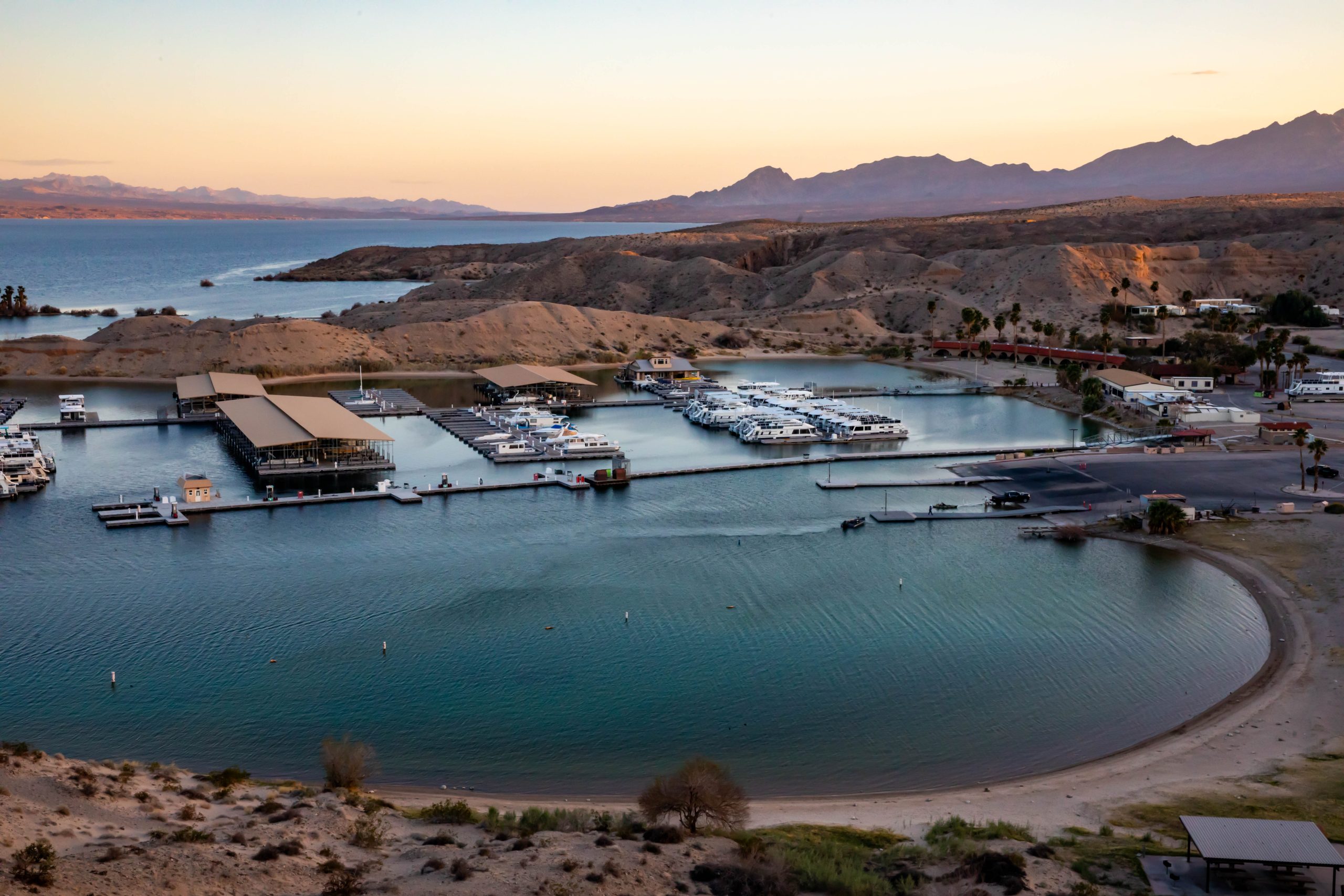 Wide aerial view of a lakeside marina with boats and surrounding hills.